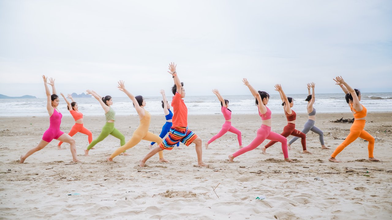 Một lớp Yoga đông học viên cùng vươn tay lên trong tư thế Chiến binh trên bãi biển