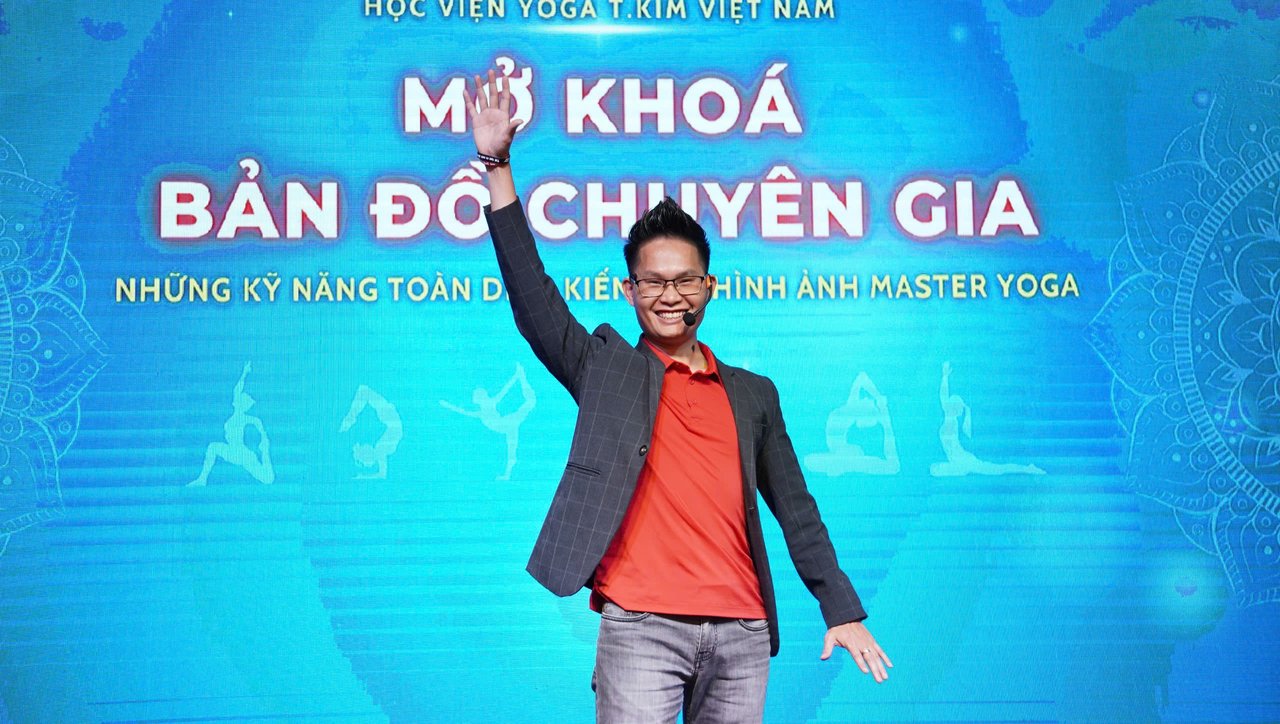 Đặng Kim Ba giơ tay chào trên sân khấu một sự kiện của Học viện Yoga T.Kim