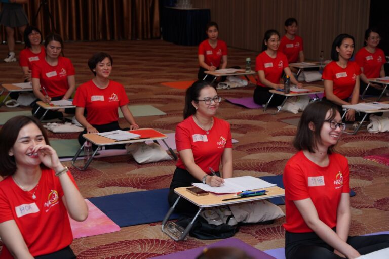 Học viên khoá đào tạo huấn luyện viên Yoga ngồi trên thảm, dùng bàn học thấp để ghi chép trong buổi học lý thuyết